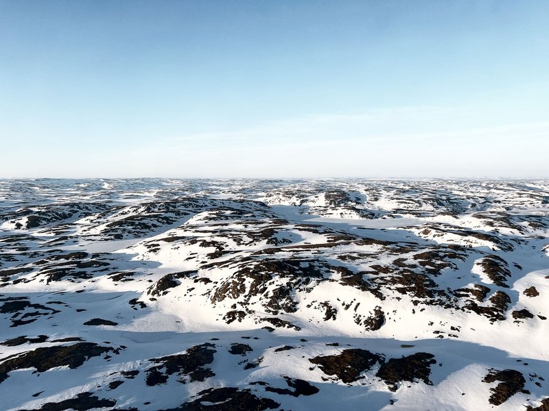 Vast arctic tundra landscape with snow-covered hills under a clear blue sky during winter.