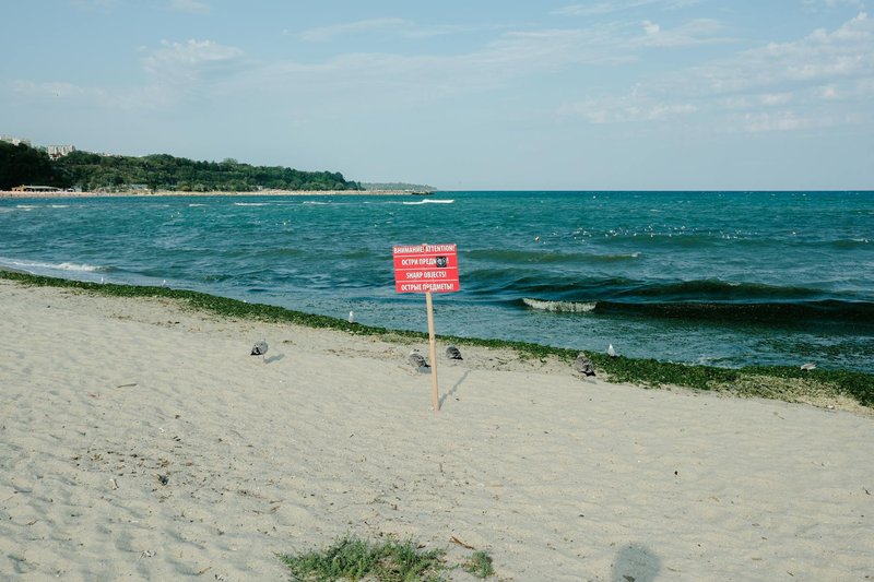 A peaceful Bulgarian beach with a warning sign about sharp objects, highlighting the serene coastal landscape.