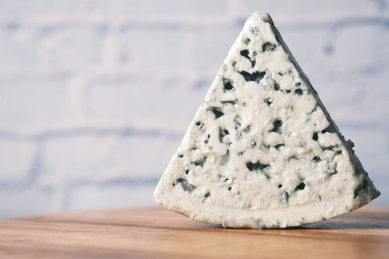A detailed close-up of a creamy stilton cheese resting on a wooden surface, emphasizing texture.