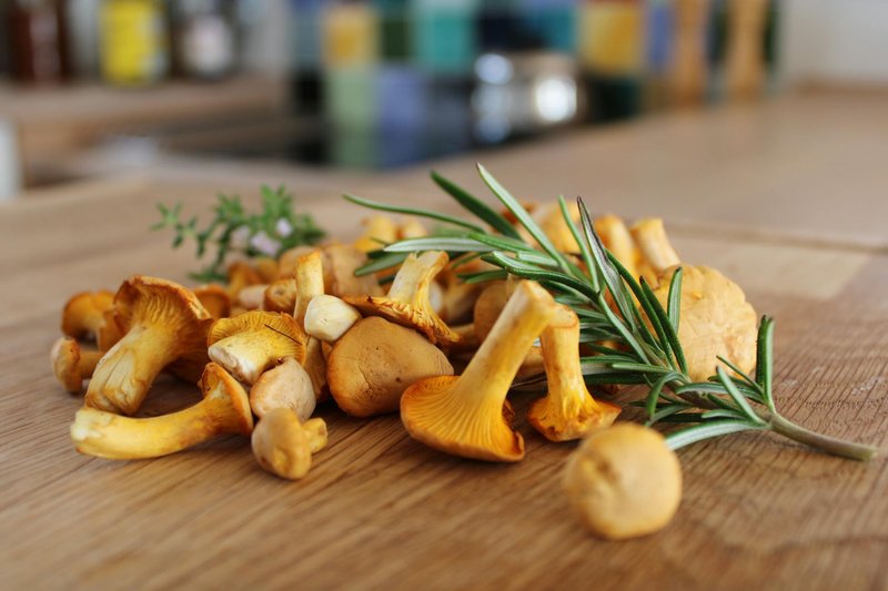Close-up of fresh chanterelle mushrooms and rosemary sprigs on a wooden table, ideal for cooking.