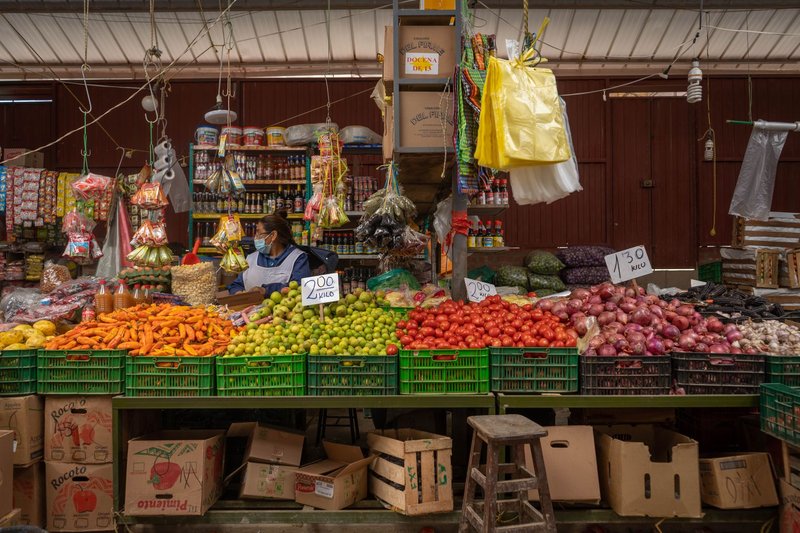 Colorful display of fruits and vegetables in a Peruvian market stall with a vendor.