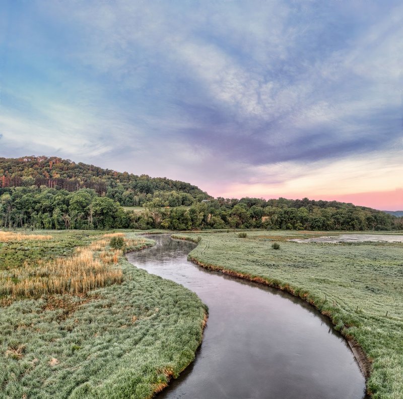 A tranquil river meanders through a lush valley at dusk under a dramatic sky.