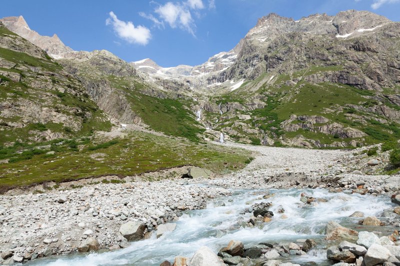 Stunning view of a clear stream flowing through the Alps under a blue sky in France.