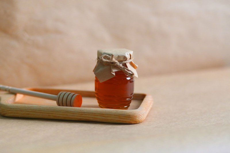A homemade jar of honey with a rustic wrapping on a wooden tray, showcasing natural sweetness.