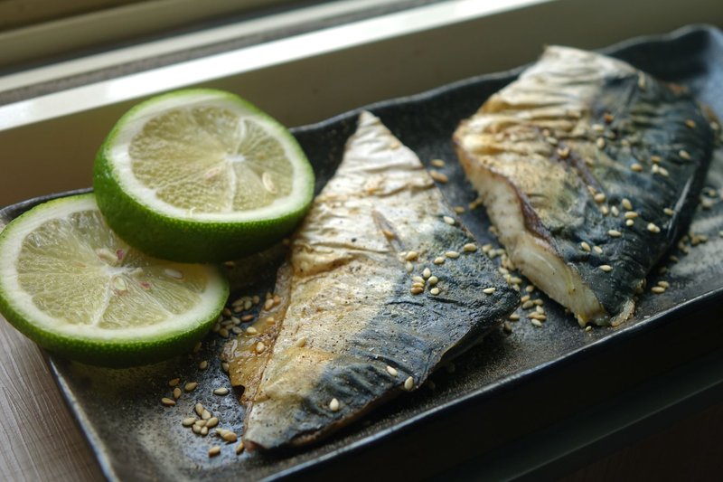 Delicious grilled mackerel served on a plate with lime slices and sprinkled sesame seeds.