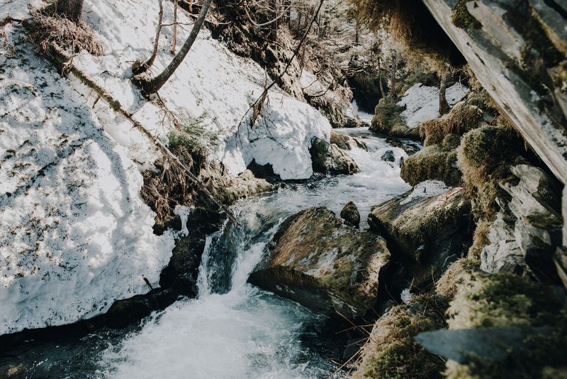 Breathtaking view of a snow-covered mountain stream with mossy rocks in Whittier, Alaska.