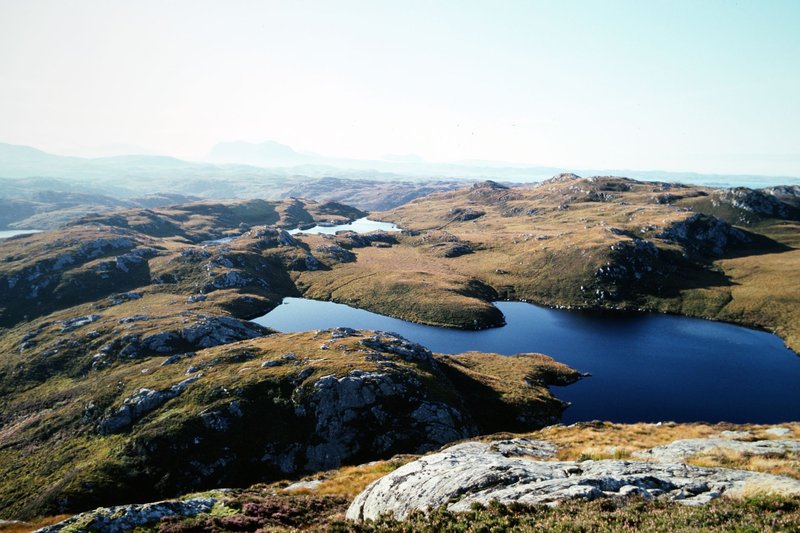 A breathtaking aerial view of the rugged landscape in the Scottish Highlands, featuring lakes and rocky terrain.