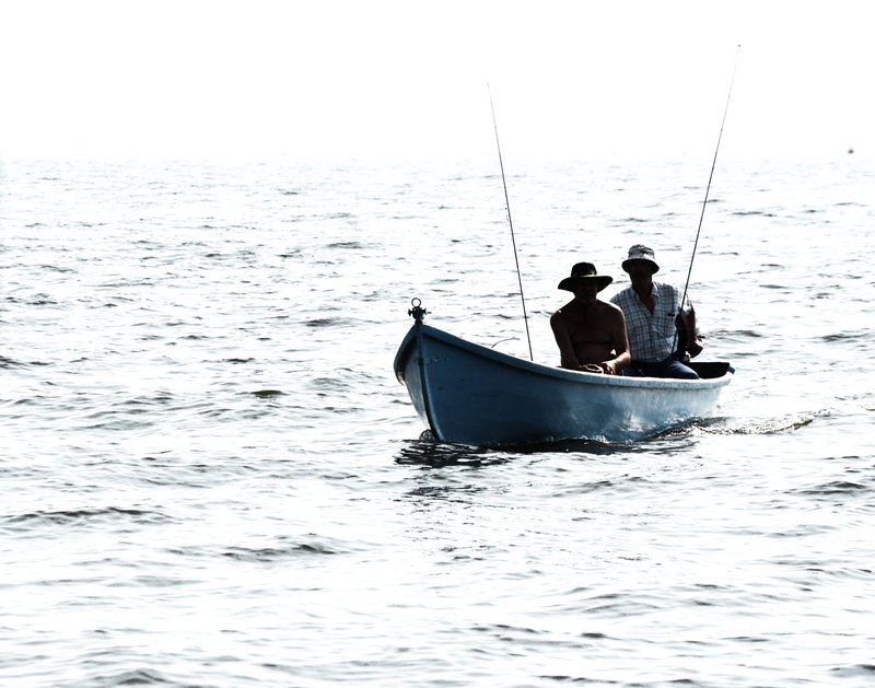 Silhouetted fishermen in a boat fishing in the tranquil open sea.