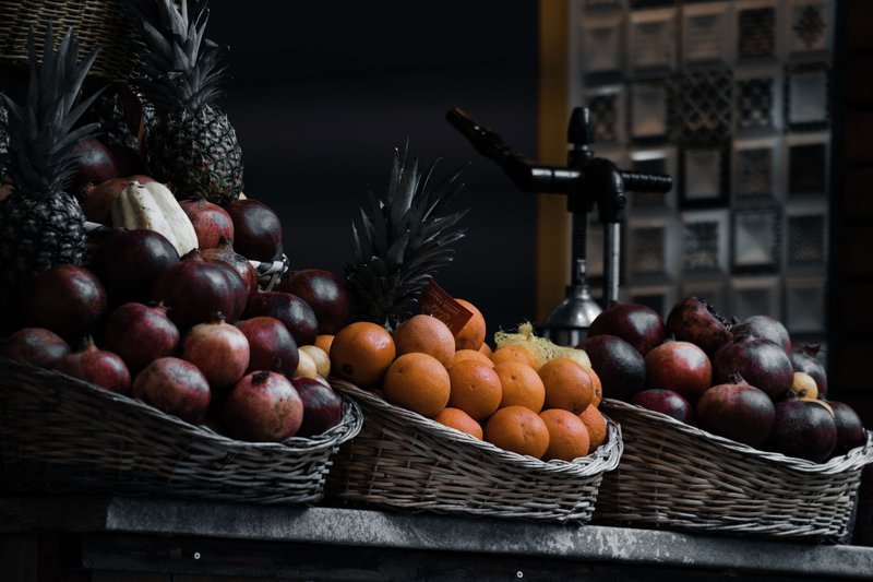 A colorful display of fruit baskets with pineapples, pomegranates, and oranges outdoors.