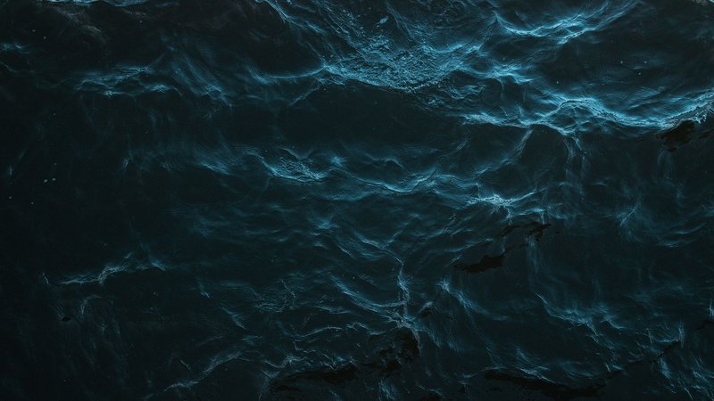 Mysterious dark ocean surface with subtle light reflections and deep blue hues.