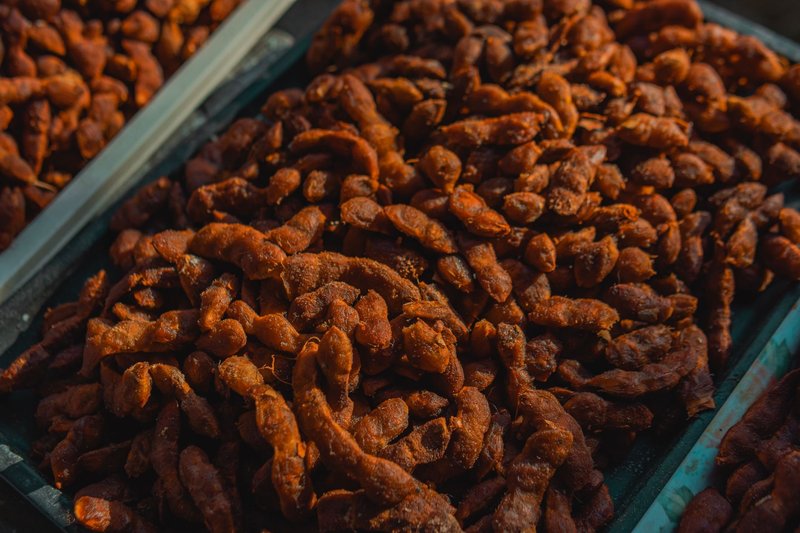 A detailed view of dried tamarind pods displayed in trays at an outdoor market, highlighting texture.