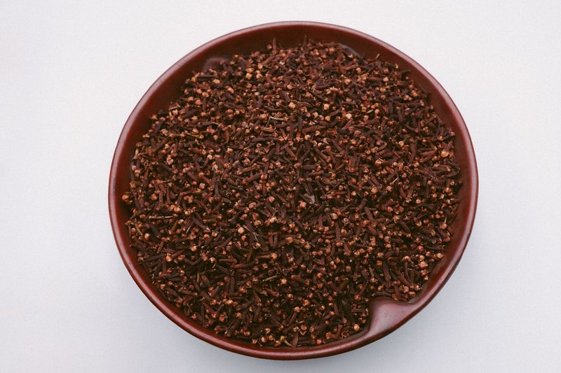 Aromatic cloves in a brown ceramic bowl from Malang, Indonesia, photographed from above.