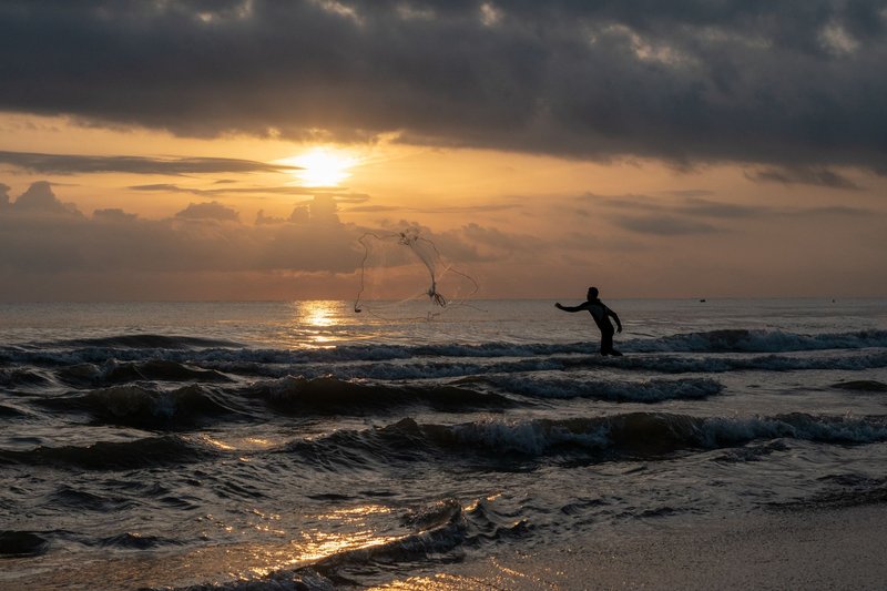 A serene sunset scene with a fisherman casting a net, creating a stunning seascape silhouette.