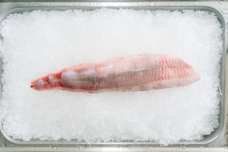 Top view of a fresh fish fillet on ice in a metal tray, emphasizing freshness and quality.