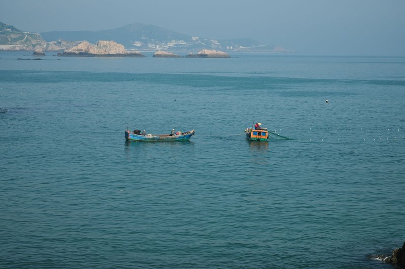 Fishing boats with nets cast on a tranquil blue sea with a distant coastal view.