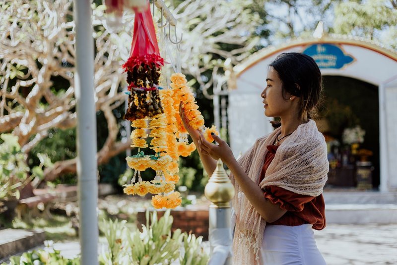 A woman observes traditional flower garlands in a sunlit outdoor setting, creating a serene ambiance.