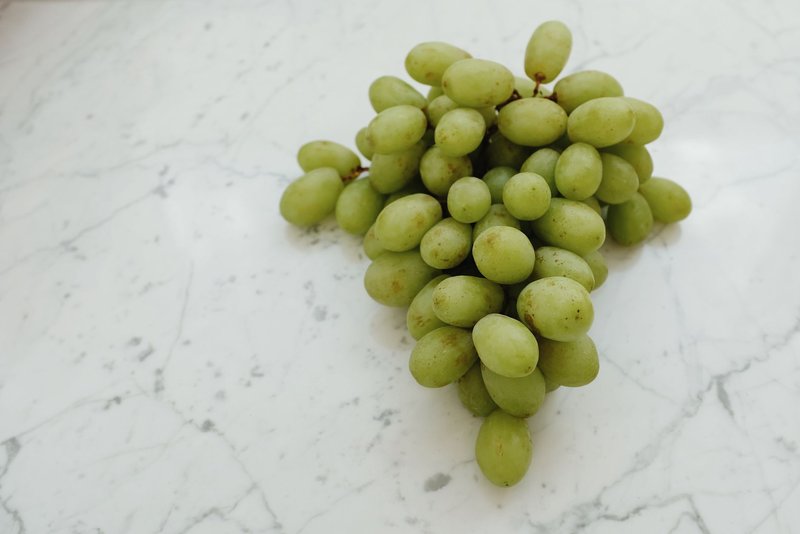 A bunch of fresh green grapes displayed on a marble tabletop, showcasing their vibrant color and freshness.