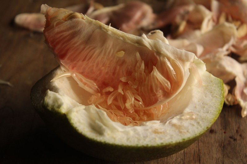 Detailed view of a peeled pomelo revealing its juicy interior resting on a wooden table.