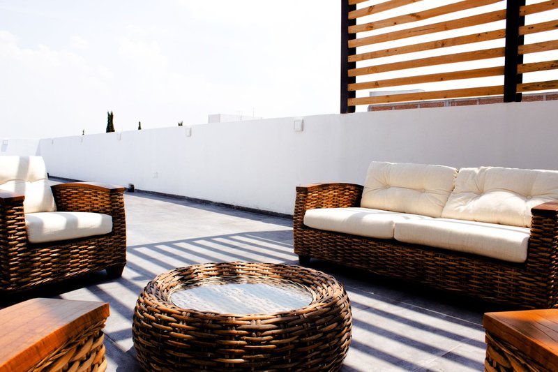 Sunny rooftop terrace with stylish wicker furniture and neutral cushions.