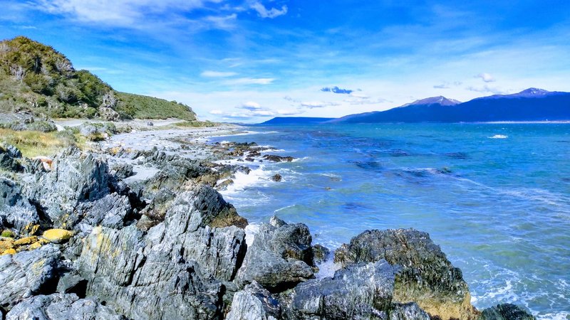 Explore the rocky seacoast of Ushuaia, Argentina, with stunning views of the ocean and distant mountains.