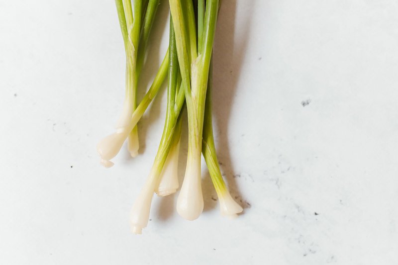 Top-down view of fresh green spring onions on a clean white surface, ideal for culinary themes.