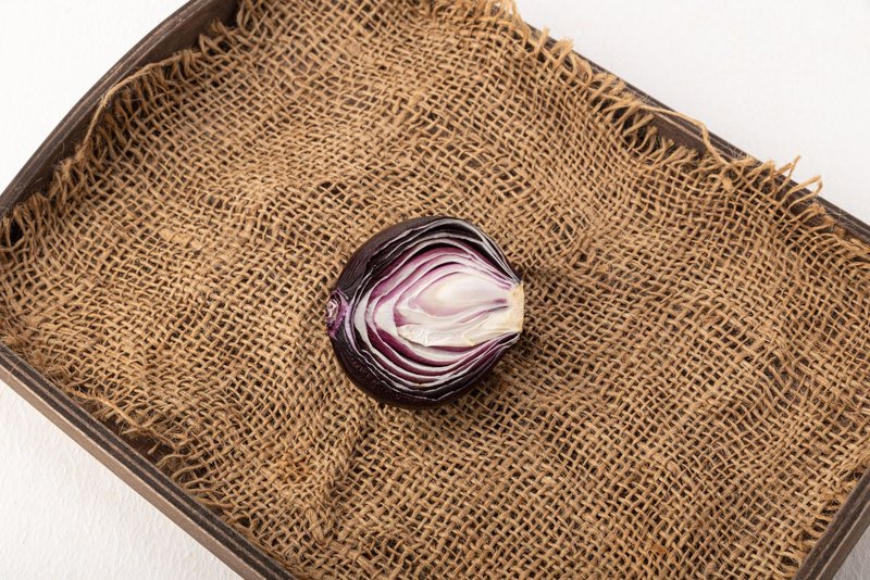 Close-up of a sliced red onion resting on a rustic burlap mat in a wooden tray.