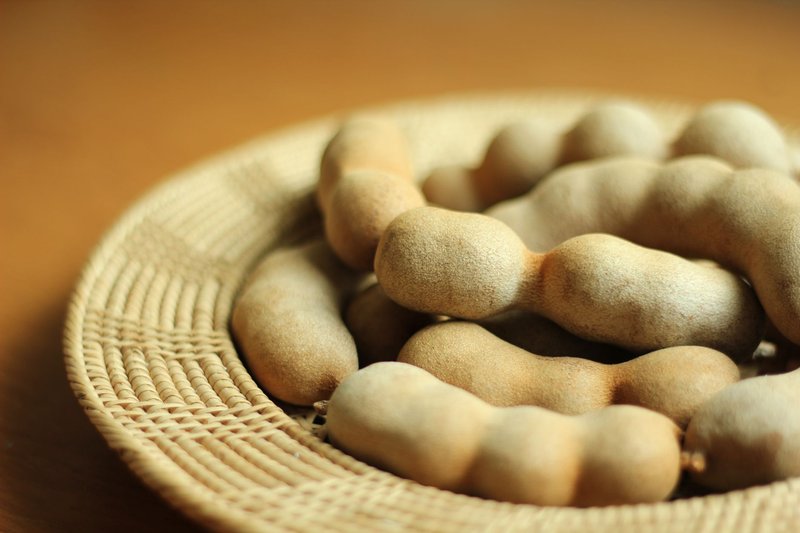 A close-up of ripe tamarind fruit in a traditional woven basket, highlighting texture and color.
